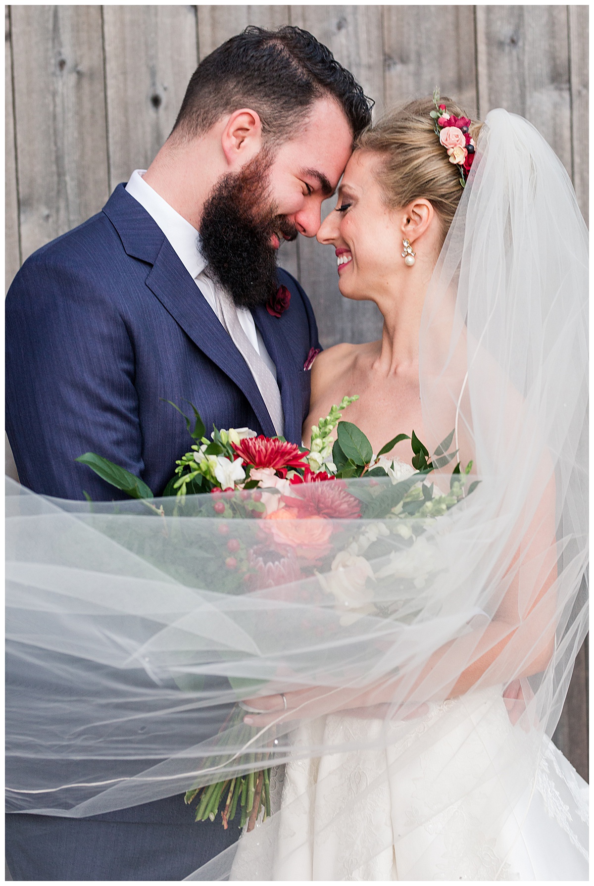 Bride and Groom embrace one another, forehead-to-forehead, with veil draped in front of them