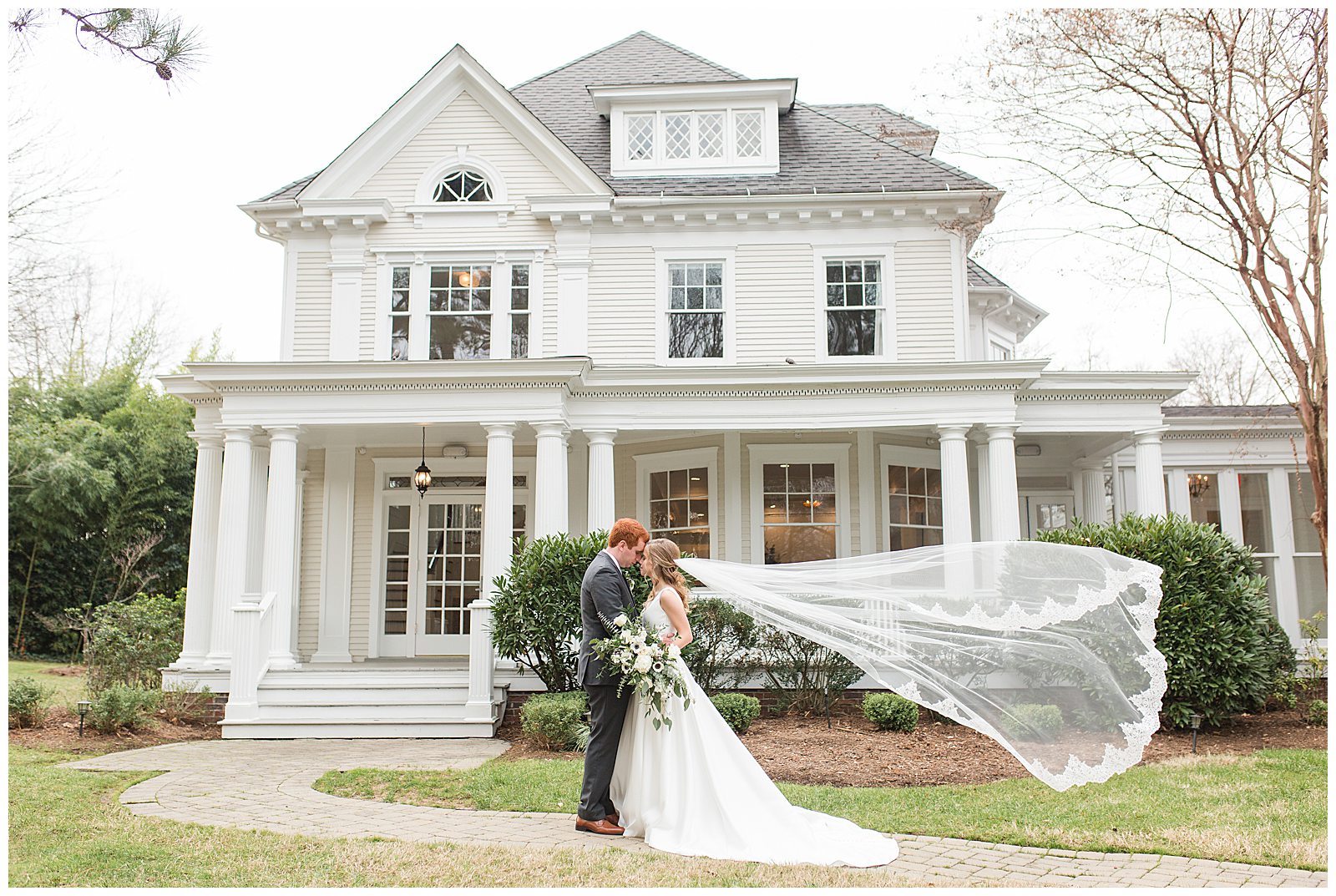 veil blows in the wind as couple poses in front of McAlister House, a historic Greensboro NC wedding venue