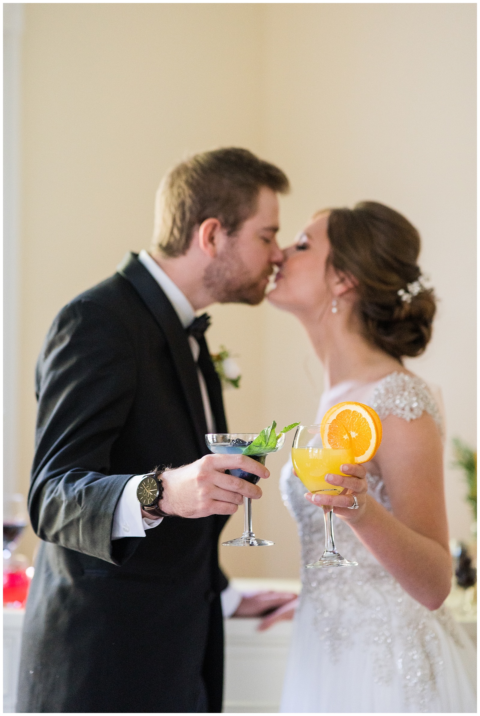 couple share a kiss and clink glasses containing colorful signature cocktails during small wedding toast
