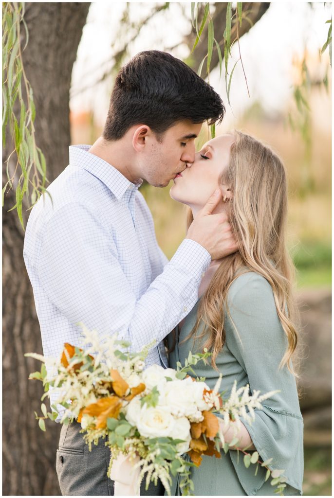 engagement portrait of couple sharing kiss under weeping willow tree in NC