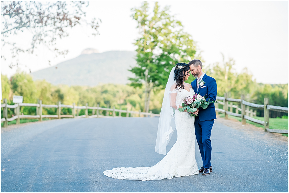 Bride and groom lean into one another with pilot mountain and Jolo Vineyards behind them