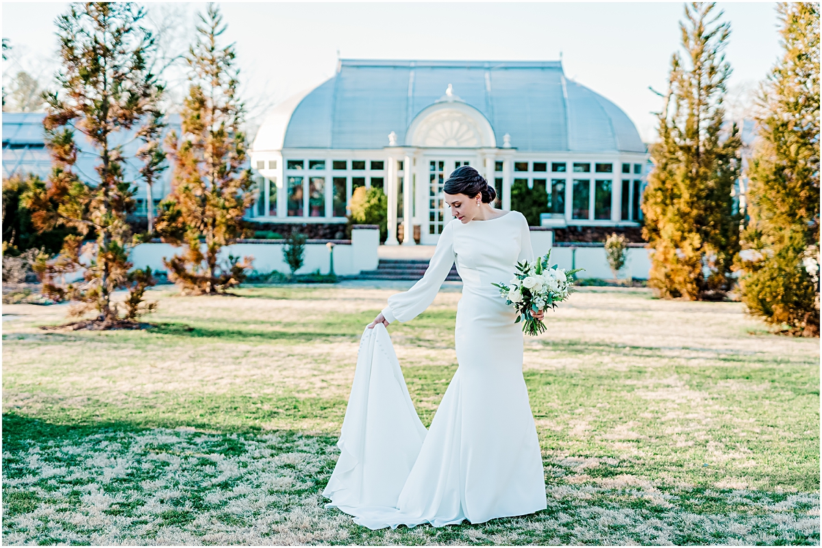 Eleanor standing in the garden in front of the greenhouse, holding train during Reynolda Gardens Bridal Session