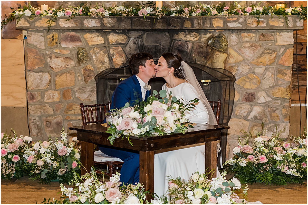 Eleanor and Justin kissing in front of fire place at the barn