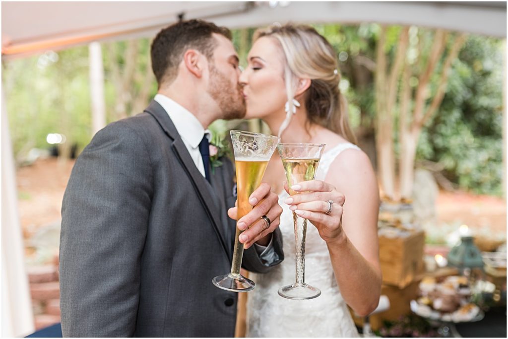 Amber and Chase kissing behind their champagne glasses during their Greensboro wedding