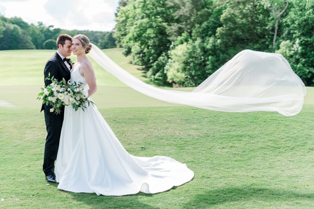 Dramatic photo off the bride's veil flying in the wind while the groom nestles in to her cheek during their Wedding in Raleigh NC
