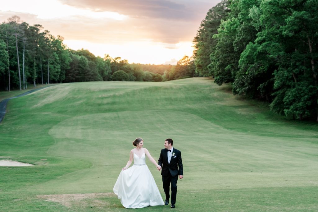 Dramatic photo of the bride and groom walking hand in hand across Washington Duke Inn and Golf Club during a gorgeous sunset.