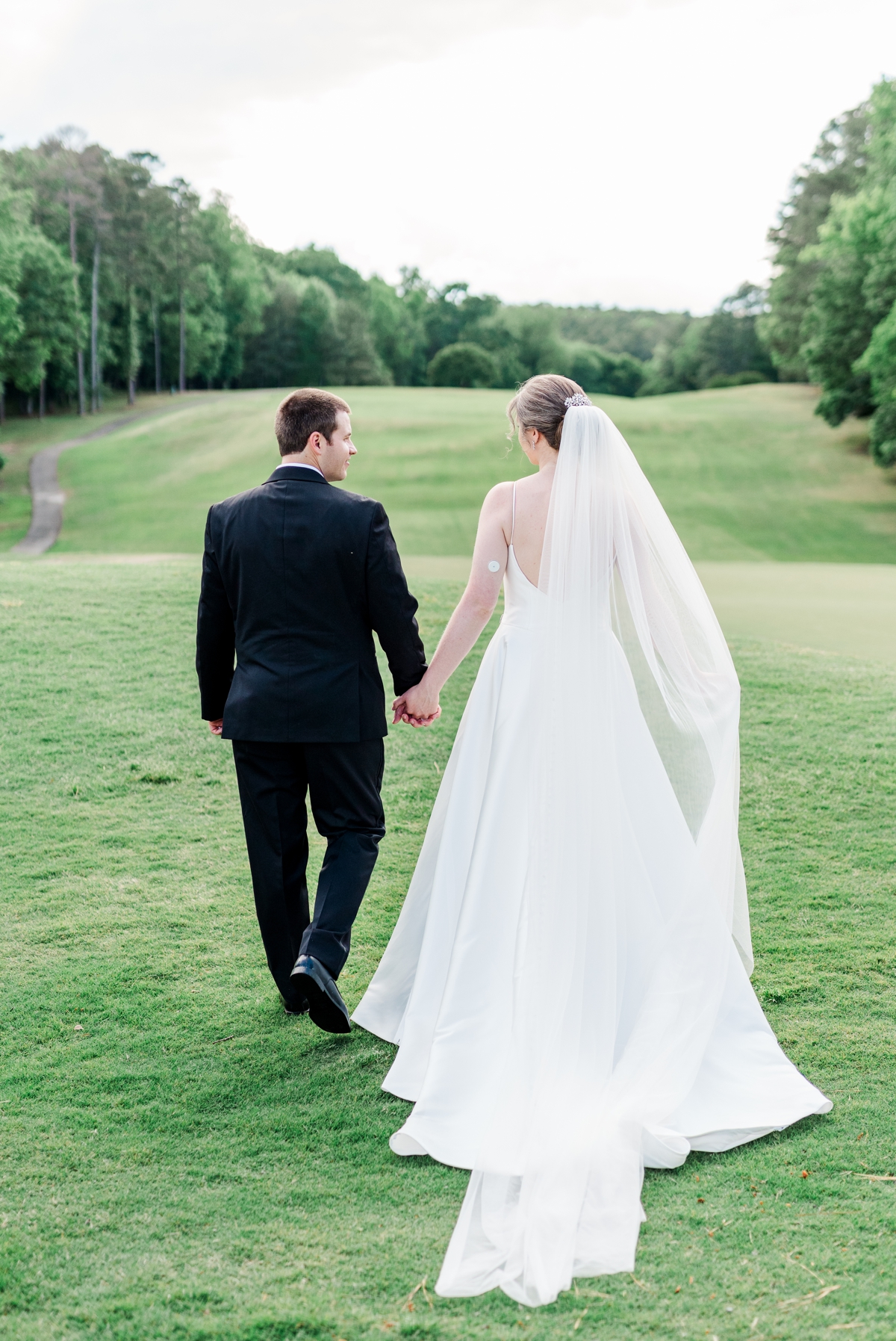 The bride and groom walking hand in hand off across the golf course during their wedding in Raleigh, NC.