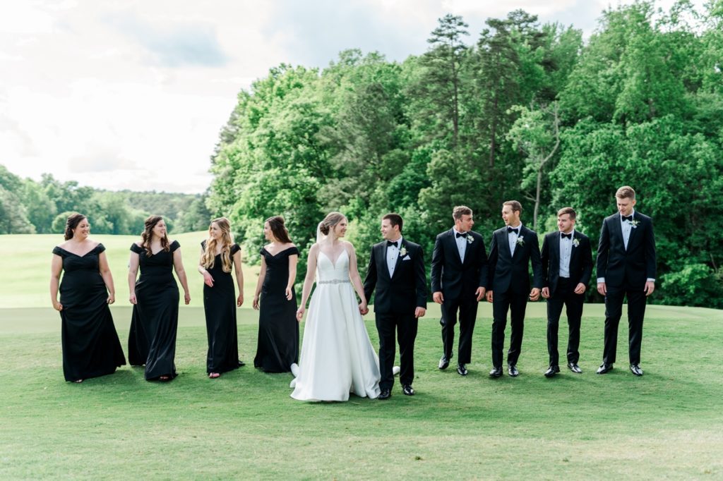 Haley and Matt walking across a golf course during their wedding in Raleigh, NC with their wedding party. 