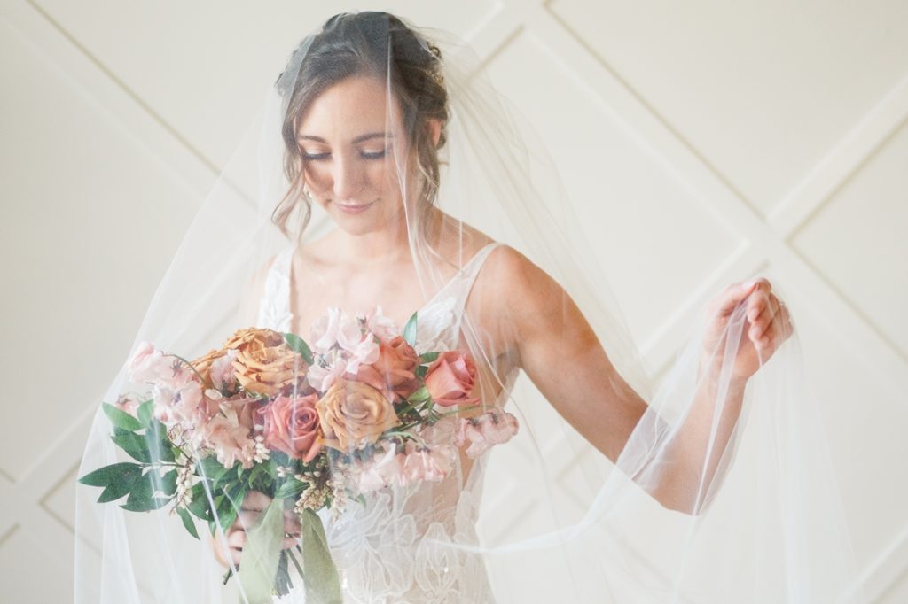 A woman in front of an accent wall with her veil over her face and her bouquet.