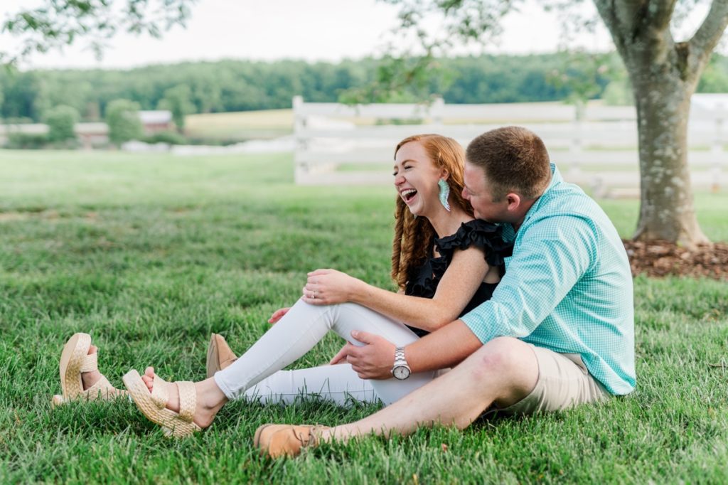 A woman sitting and laughing in her fiance's lap at Adaumont Farm while her fiance hugs her.
