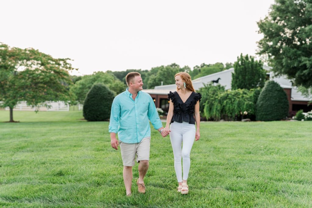 A man and woman walking hand in hand as they smile at each other during their engagement session.