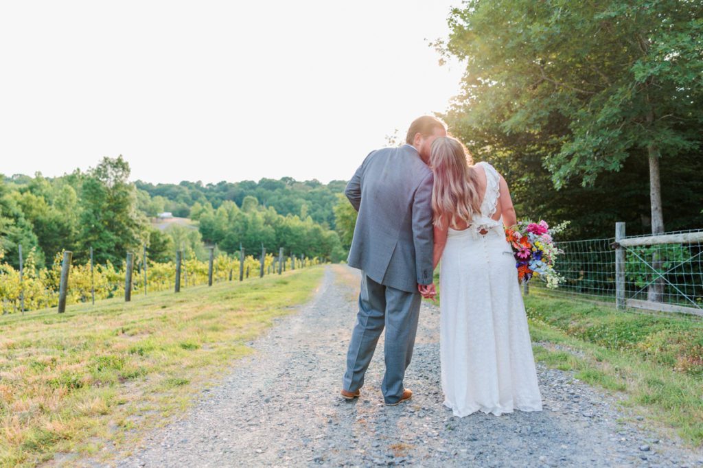 A bride and groom kissing with their backs turned in a vineyard at Medaloni Vineyards.