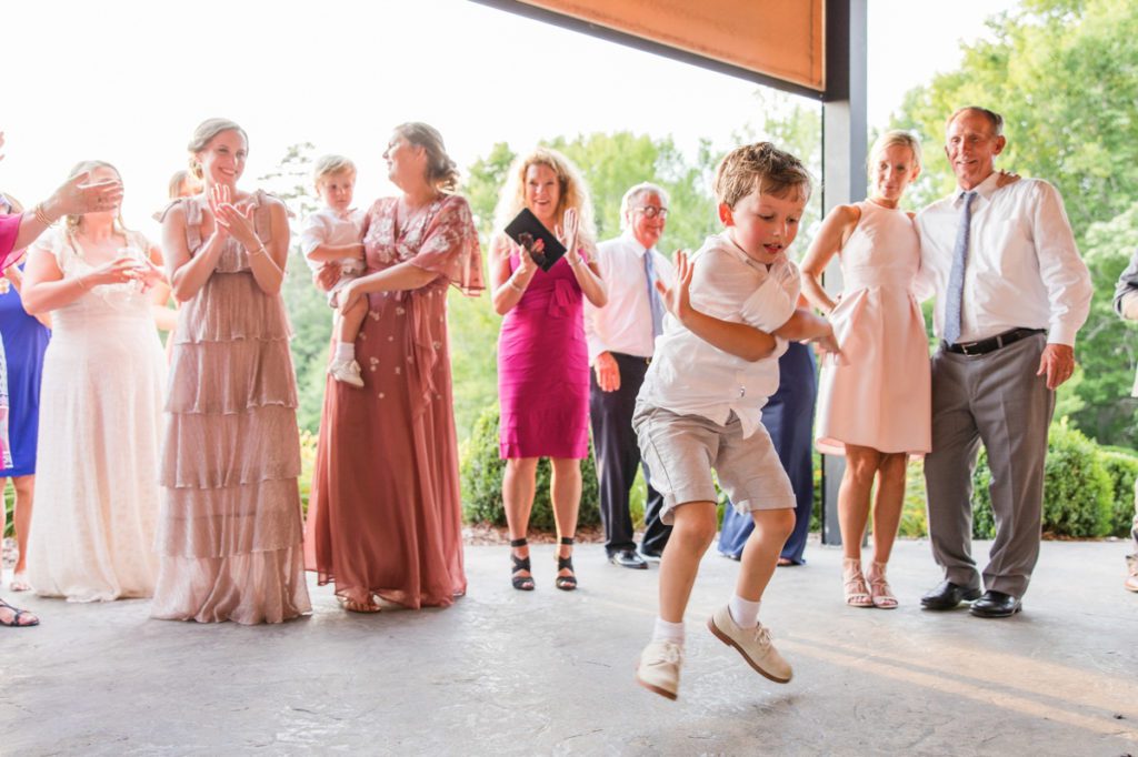 A little boy dancing during a wedding reception while other guests cheer him on.