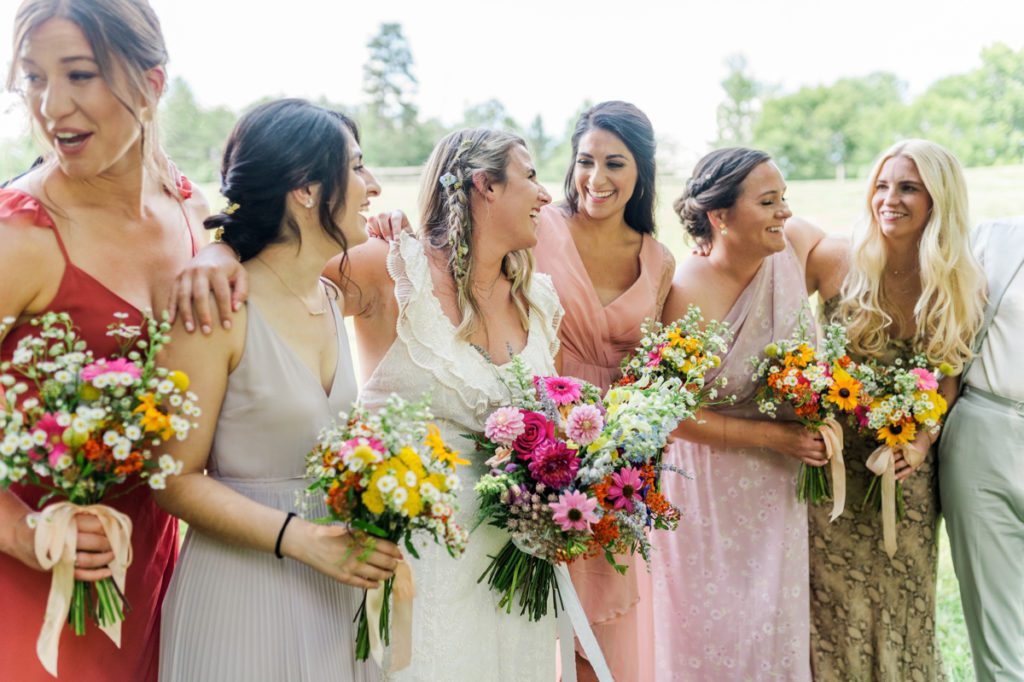 The bride laughing with her bridesmaids in field on her wedding day.