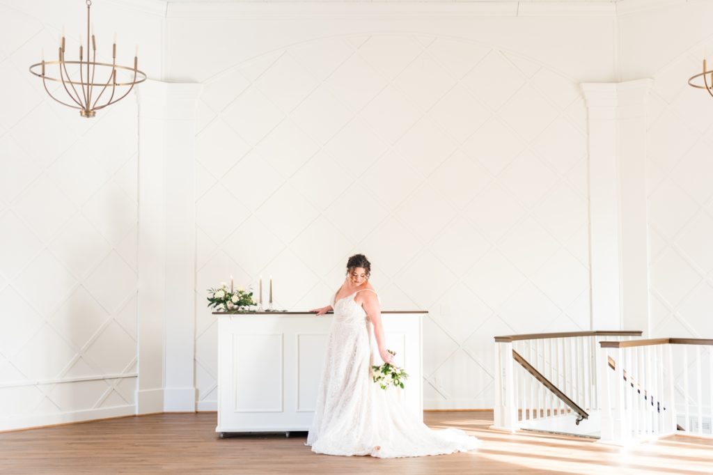 A bride looking down at her bouquet on the upper floor of white wedding venue Blandwood Carriage House.