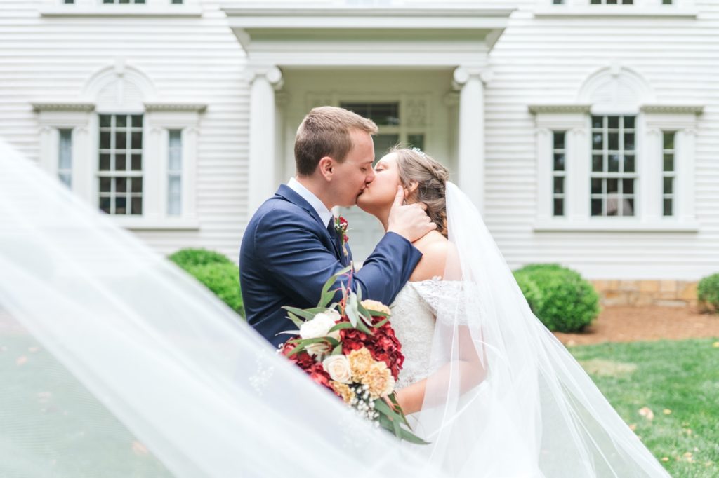 A bride and groom kissing in front of white wedding venue, Holt House.