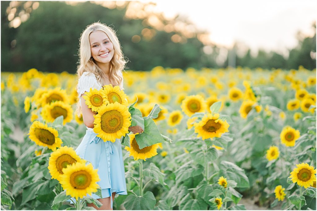 Senior posing for senior pictures in a field of sunflowers at Sunflower Extravaganza - known as one of the best locations for photography in North Carolina 