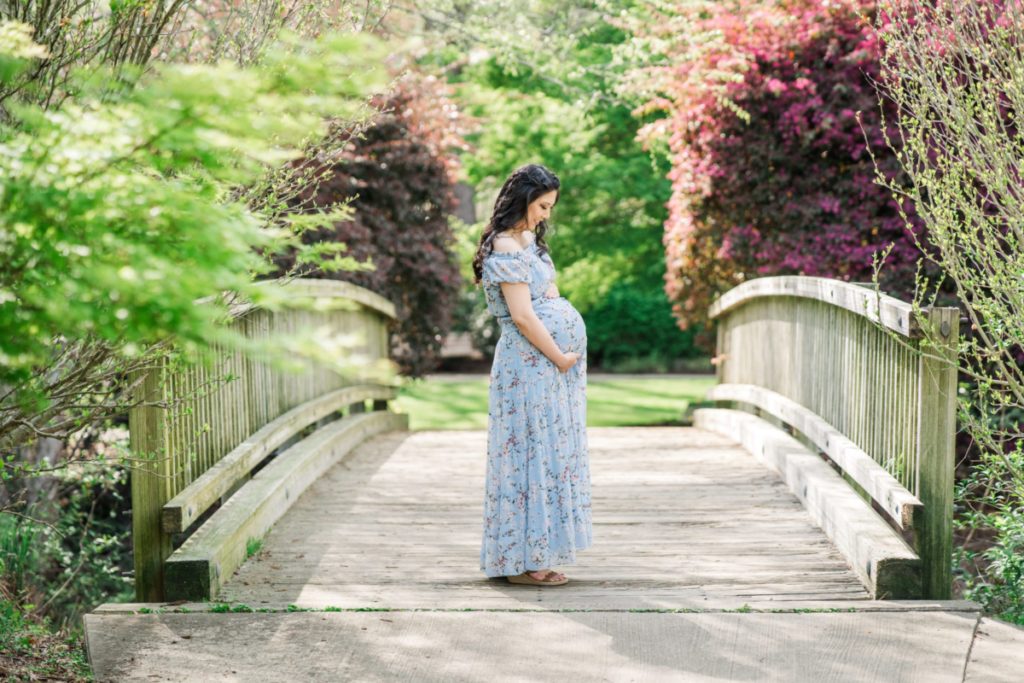 An expecting mother standing on a park bridge in Greensboro embracing her belly.