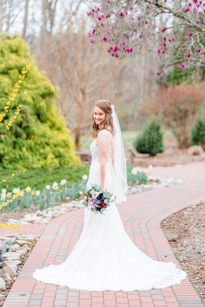 Bride looks over her shoulder surrounded by blooming trees and plants in Winston-Salem, NC.